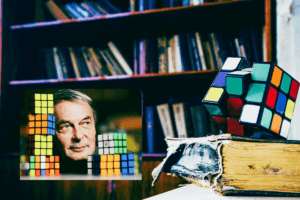 Imagem de Erno Rubik olhando em direção a sua invenção, num estilo vintage, ilustrando a origem do cubo mágico.