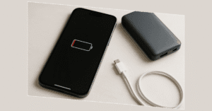 iPhone com bateria fraca ao lado de um carregador portátil, ilustrando a necessidade de aprender como economizar bateria do iPhone.